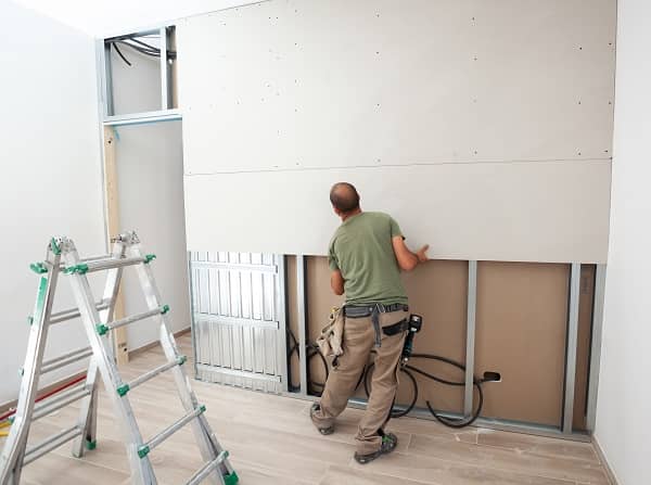 Worker building plasterboard wall. Working with cutting tools, fixing and measuring for drywall.