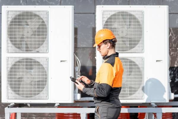 Workman in front of air source heat pumps Workman servicing air source heat pumps with an interactive tablet