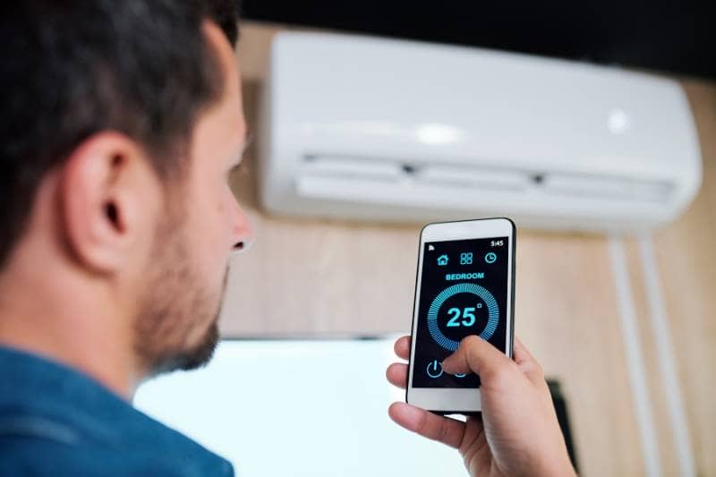 Man controlling bedroom temperature with mobile phone linked to smart heating system